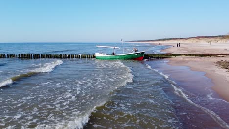 Schöne-Luftaufnahme-Eines-Roten-Raupentraktors-Und-Eines-Grünen-Fischerbootes-An-Der-Küste,-Das-An-Sonnigen-Tagen-Am-Alten-Hölzernen-Pier-Angedockt-Ist,-Ruhiges-Meeresufer,-Weitwinkel-drohnenschuss-In-Niedriger-Höhe,-Der-Sich-Vorwärts-Bewegt