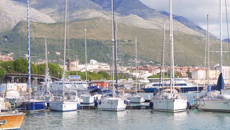 Gorgeous-scenic-view-of-coastal-Gaeta-seaport-with-large-sailboats-and-boats-docked-at-marina-with-downtown-cityscape-and-colorful-mountains-in-background,-Italy,-static