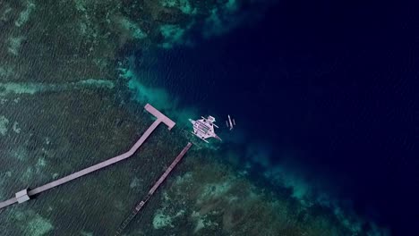 Jukung-boat-seen-from-above-in-Raja-Ampat-islands-Indonesia-on-a-coral-reef-pier-diving-spot,-Aerial-top-view-lowering-shot
