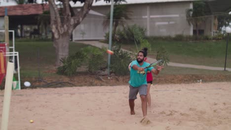 Male-beach-tennis-player-defending-attack-with-backhand-in-sand-court