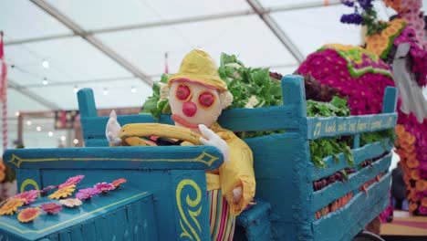 Royal-Cornwall-Show-2019---Agricultural-Farm-Exhibit---A-Farmer-Doll-With-His-Fresh-Farm-Vegetables-Being-Loaded-On-A-Blue-Wooden-Truck---Medium-Shot