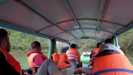 Barco-Turístico-Con-Gente-Con-Chalecos-Salvavidas-Acercándose-A-La-Entrada-De-La-Caverna-Debajo-De-La-Montaña,-Toma-De-Mano