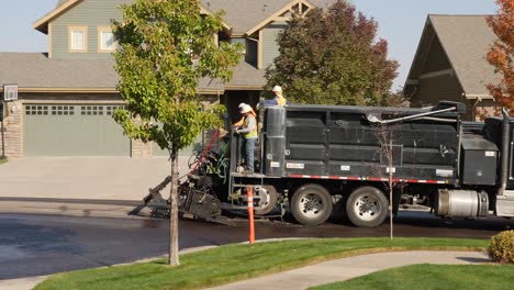 Asphalt-truck-backing-up-a-hilling-neighborhood-street-with-crew-on-back