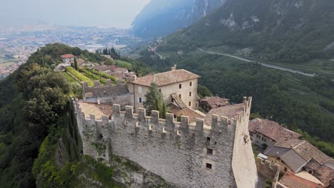 Old-Medieval-Castle-on-Hilltop-Above-Riva-Del-Garda-City,-Italy,-Trento-Province-Aerial-View-of-Castello-di-Tenno-Landmark-on-Sunny-Summer-Day