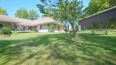 POV-driving-small-tractor-driving-across-a-large-yard-past-a-garden-toward-the-house-and-barn