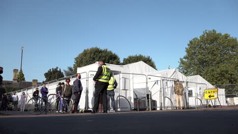 A-man-is-directed-into-an-appointment-only-Covid-19-testing-centre-by-a-security-guard-as-others-queue-in-protective-face-masks-queue-outside