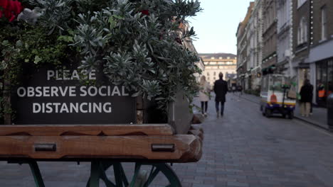 Menschen-Gehen-An-Einem-Schild-Auf-Einem-Dekorativen-Handkarren-Vorbei,-Auf-Dem-Steht:-„Bitte-Beachten-Sie-Die-Soziale-Distanzierung“-In-Einem-Sehr-Ruhigen-Covent-Garden-Während-Der-Zweiten-Nationalen-Sperrung-Des-Coronavirus