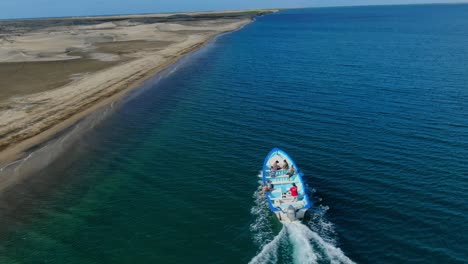 Vista-Aérea-Inclinándose-Hacia-Arriba,-Barco-Turístico-Moviéndose-A-Lo-Largo-De-La-Costa-De-La-Purísima-Baja-California-Sur,-México,-Cielo-Azul-Brillante-En-El-Fondo