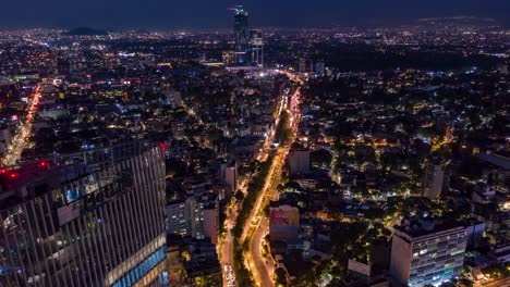 Aerial-flyover-of-Manacar-Tower-Roundabout-at-night-Traffic-in-Mexico-City,-Timelapse-from-above-the-tower