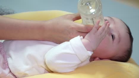 Koreanisches-Baby,-Das-Von-Der-Mutter-Mit-Flaschennahrung-Gefüttert-Wird,-Während-Es-Auf-Einem-Gelben-Kissen-Liegt
