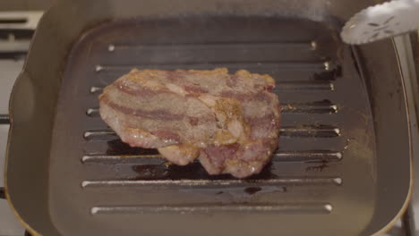 Half-cooked-ribeye-steak-being-flipped-in-grill-pan