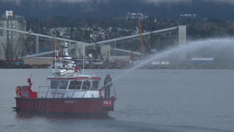 Ein-Feuerlöschboot,-Das-Eine-Wasserfontäne-Sprüht,-Während-Es-Sich-Langsam-Am-Seehafen-Vorbeibewegt---Mittlere-Einstellung,-Zeitlupe