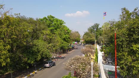 Wat-Phra-Phutthabat,-Saraburi,-Tailandia,-Imágenes-Aéreas-Constantes-De-4k-De-Una-Comunidad,-Entrada-Al-Templo-Budista,-Una-Bandera-Tailandesa,-Luces-De-La-Calle,-Cruce-De-Personas,-Automóviles-Y-Motocicletas-Que-Pasan