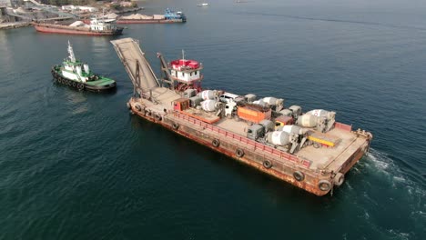 Barge-loaded-with-Concrete-mixer-trucks-pulled-to-port-by-a-Tugboat-in-Hong-Kong-bay,-Aerial-view