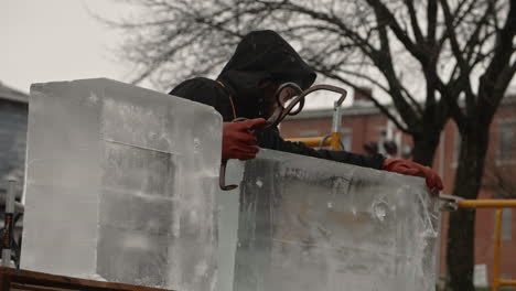 Sculptor-sliding-ice-block-off-of-pallet-and-into-position-with-falling-snow,-Slow-Motion