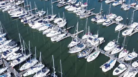 Flying-above-luxury-yachts-and-sailboats-reflections-on-sunny-Conwy-marina-birdseye-aerial-rising-view