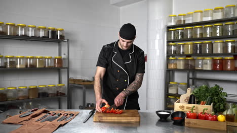 Tattooed-chef-in-a-black-chef-outfit-slicing-peppers-in-a-kitchen