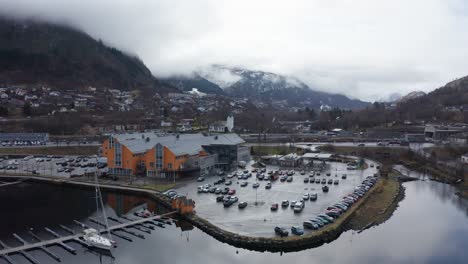 Reverse-Aerial-showing-Oyrane-Torg-and-Arna-shopping-centre-with-parking-lot,-road,-sailboat-marina-and-salmon-river---Dusk-morning-light