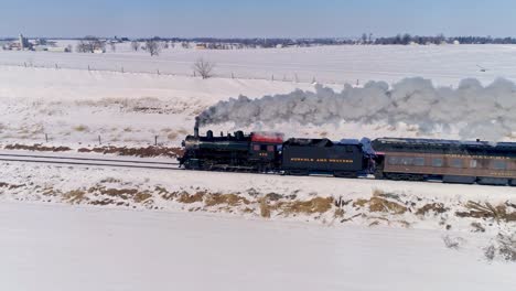 Aerial-View-of-an-Antique-Steam-Locomotive-Approaching-Pulling-Passenger-Cars-and-Blowing-Smoke-and-Steam-After-a-Snow-Storm