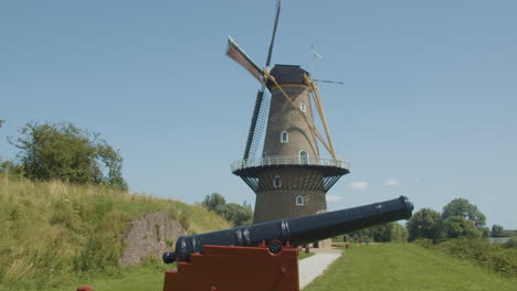 Weitwinkelaufnahme-Einer-Traditionellen-Windmühle,-Die-Sich-Dreht,-Mit-Einer-Schwarzen-Kanone-Im-Vordergrund