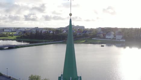 Bright-sunlight-on-lake-Tjörnin-with-bell-tower-and-cross-of-Frikirkjan-church