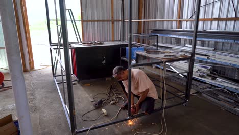 Indonesian-man-grinding-metal-frame-with-angle-grinder,-handheld-view