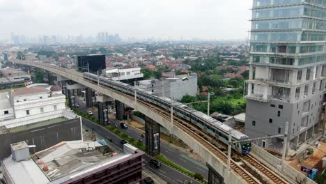 MRT-train-on-high-tracks,-road-traffic-and-skyline-of-Jakarta,-aerial