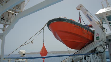 Orangefarbenes-Rettungsboot,-Das-An-Einem-Schiffskran-Befestigt-Ist,-Der-Im-Sommer-über-Das-Meer-Segelt