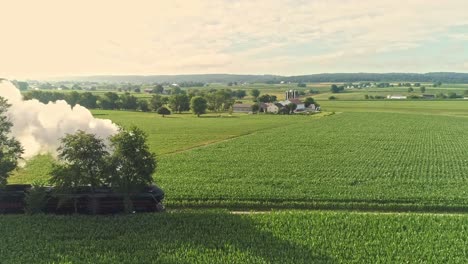 Paisaje-Aéreo-De-Tierras-De-Cultivo-Y-Un-Motor-De-Vapor-Antiguo-Pasa-A-Través-De-Los-Campos-De-Maíz-En-Una-Mañana-De-Verano-Temprano