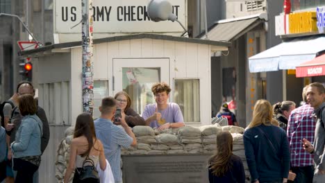 Two-happy-teens-taking-a-picture-in-front-of-the-Checkpoint-Charlie-monument-in-Berlin,-Germany