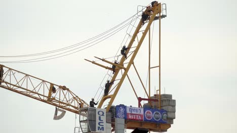 Una-Foto-De-Un-Equipo-De-Trabajadores-De-La-Construcción-Tailandeses-Suspendidos-Del-Marco-De-Una-Grúa,-Los-Hombres-Trabajan-Para-Ensamblar-Y-Manipular-El-Equipo-En-Un-Nuevo-Sitio-De-Construcción-Urbana-En-Bangkok,-Tailandia