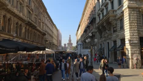 Vía-Calle-Peatonal-Dante-En-Milán-Con-Gente-Paseando-Y-Comprando-Con-El-Castillo-Sforza-En-El-Fondo,-Italia