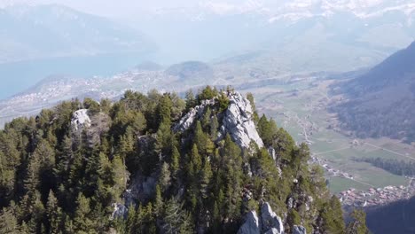 camera-pans-over-a-mountain-peak-and-aims-down-towards-the-small-swiss-mountain-village-"Wimmis",-stunning-surroundings-with-lakes-and-alps