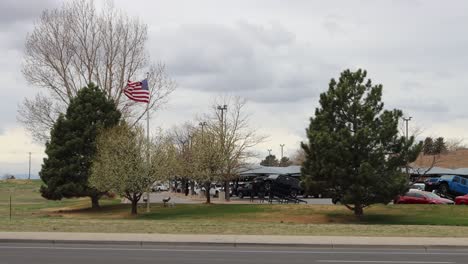 Extremer-Wind-Im-Norden-Von-Colorado-Amerikanische-Flagge-Mit-Bäumen-Und-Verkehr