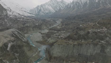 Aerial-shot-of-cinematic-view-of-the-beautiful-area-of-Attabad-Lake,-in-Gojal-Valley,-Hunza,-Gilgit-Baltistan,-Pakistan-with-beautiful-snow-clad-mountains-and-icy-river-passing-through-valley