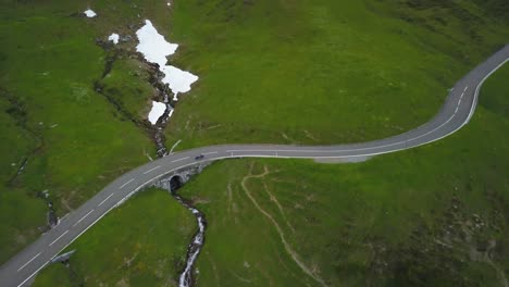Aerial-dolly-in-of-motorcyclists-riding-on-a-paved-road-in-green-Klausen-Pass-mountainside-near-Hotel-Passhohe-at-daytime,-Switzerland-Alps