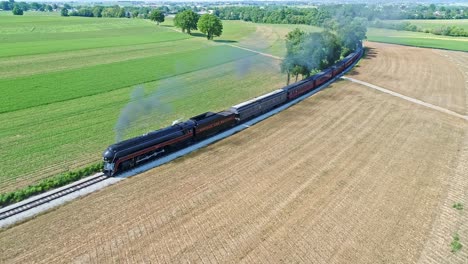 Luftaufnahme-Einer-Antiken-Dampfmaschine-Und-Personenwagen,-Die-An-Einem-Sonnigen-Sommertag-Entlang-Der-Landschaft-Fahren-Und-Rauch-Und-Drohnen-Vor-Sich-Herziehen