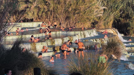 Gente-Relajándose-En-Las-Piscinas-Termales-Mientras-El-Agua-Cae-En-Cascada-A-Través-De-Los-Niveles