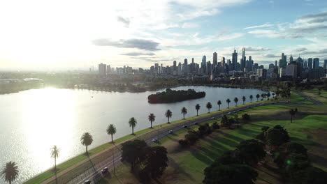 Smooth-aerial-approach-toward-Melbourne-CBD-while-traffic-leaves-the-city-area-in-a-single-file-beside-Albert-Park-Lake