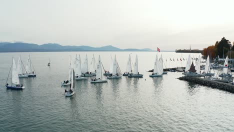 Medium-dolly-left-to-right-drone-shot-of-a-collection-of-yachts-heading-back-to-harbour-in-a-Swiss-town-with-mountains-in-the-background