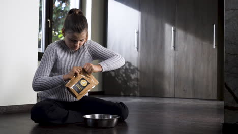Girl-on-floor-reading-pet-food-label,-opening-it,-pouring-it-into-bowl