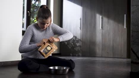 Niña-En-El-Piso-Leyendo-La-Etiqueta-De-Comida-Para-Mascotas,-Abriéndola,-Vertiéndola-En-Un-Tazón