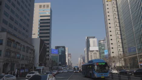 Cars-moving-on-Gangnam-daero-road,-buses-arriving-to-the-bus-stop-of-Gangnam-station-in-city-centre-daytime