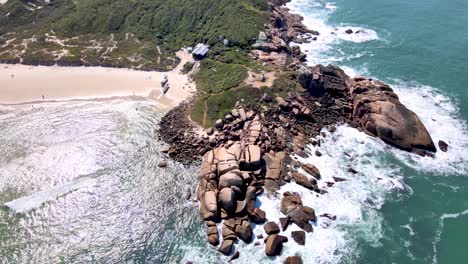 Aerial-drone-view-of-tropical-tourist-beach-with-rocks-touching-the-sea-and-sand-in-Florianópolis-magic-island