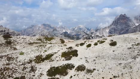 A-drone-shot-of-3-hikers-who-are-hiking-on-a-mountain-trail-with-an-outstanding-view-of-the-incredible-landscape-of-the-Dolomites-in-Italy-on-a-sunny-day
