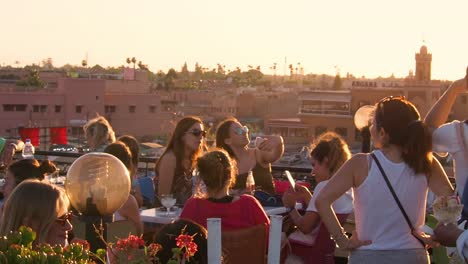 Imágenes-De-4k-De-Mujeres-Turistas-Tomando-Fotos-Con-Sus-Teléfonos-Inteligentes-En-Una-Azotea-Durante-La-Puesta-De-Sol-En-El-Mercado-Djemaa-El-fnaa,-Marrakech,-Marruecos