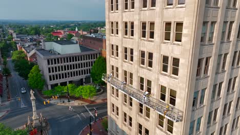 Aerial-zoom-out-reveals-Griest-Building-with-blue-collar-workers-high-upon-scaffolding