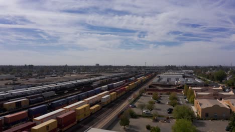 Low-aerial-shot-following-a-freight-train-passing-through-the-railyards-of-downtown-Bakersfield,-California