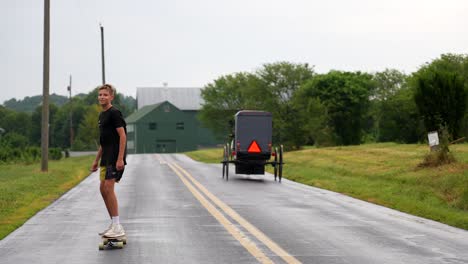 Amisches-Pferd-Und-Kutsche-Geht-An-Jungen-Vorbei,-Der-Auf-Der-Hinterlandstraße-Skateboard-Fährt