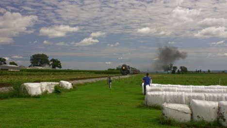A-View-of-a-Young-Family-Watching-and-Waving-as-a-Restored-Antique-Steam-Passenger-Train-Approaches-Blowing-Black-Smoke-and-Steam-on-a-Sunny-Day